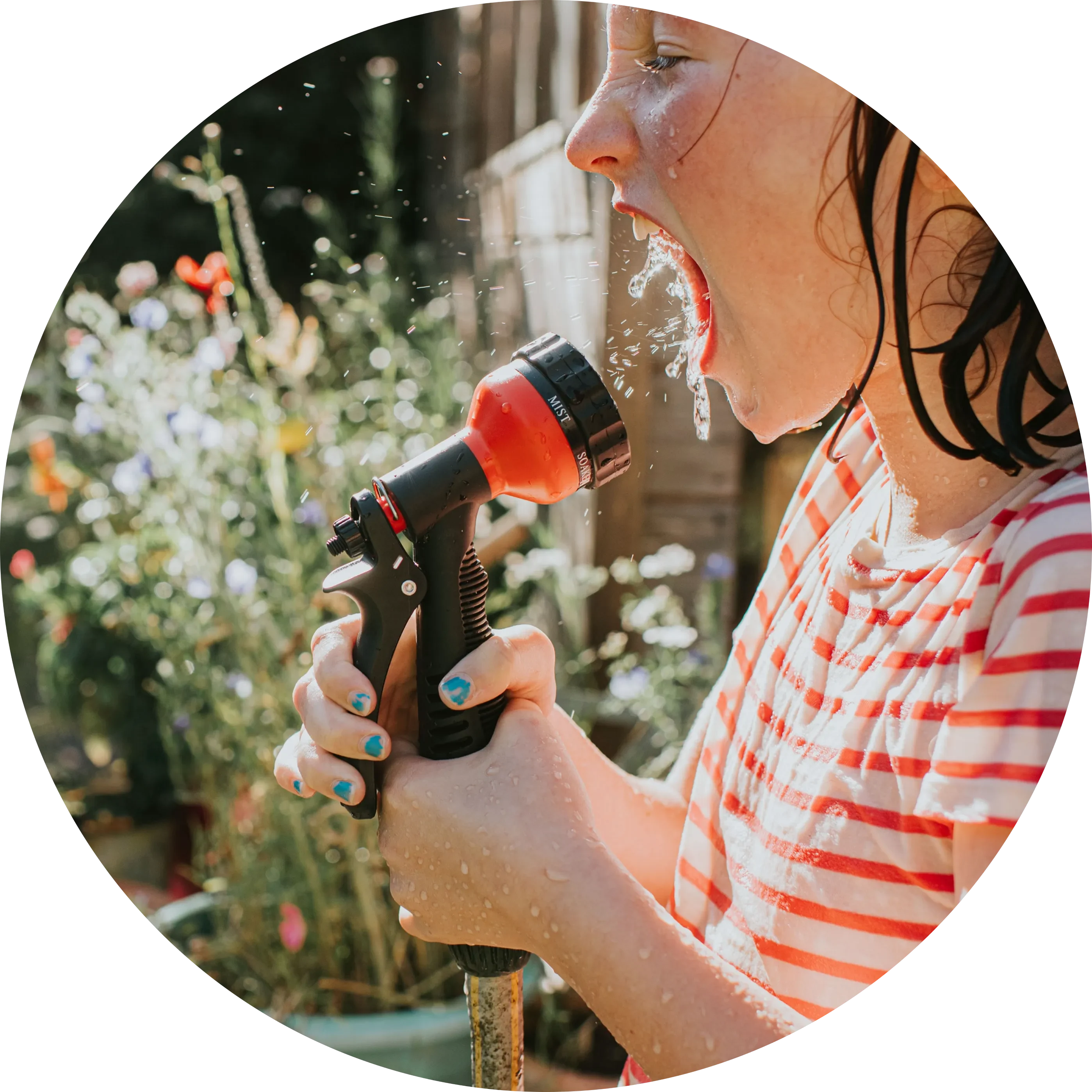 A little girl sprays water directly into her mouth using a hosepipe